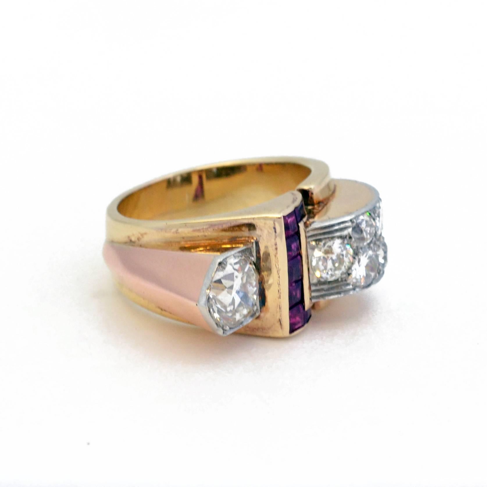 A diamond set dress ring, with stylised ruby set ‘buckle’. Mounted in 18ct yellow and rose gold, topped with platinum. American, circa 1940. Principle diamond weighs approximately 0.85ct. 

Size N.5