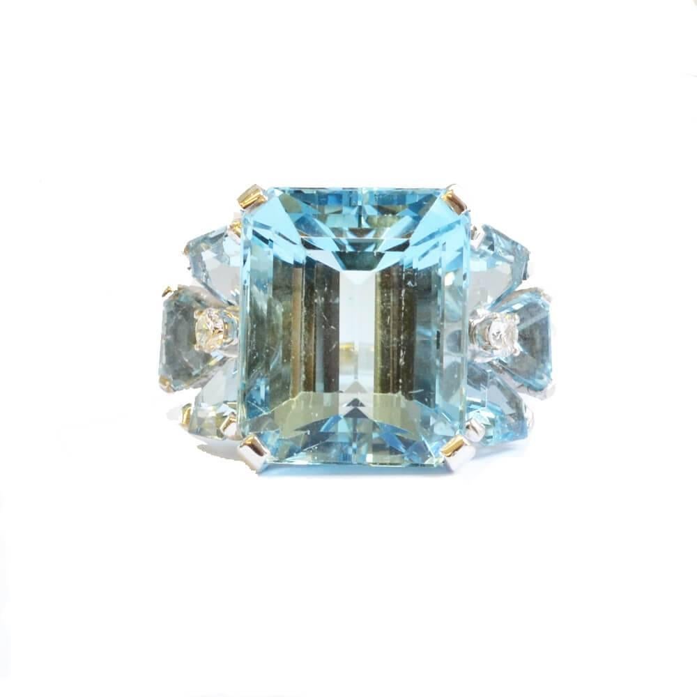 An aquamarine and diamond set cocktail ring, with a principal large aquamarine to the centre flanked by three triangular aquamarines arranged in a floral setting with diamond accents. Mounted in platinum. American, circa 1930. 