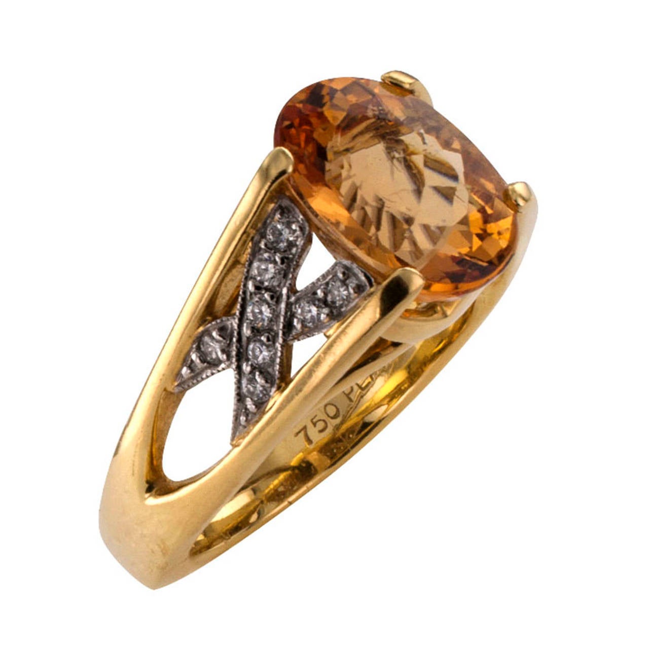Circa 1990, this eye-catching contemporary ring centers upon a very pretty oval imperial topaz weighing approximately 4.75 carats, platinum X shaped motifs set with diamonds totaling approximately 0.33 carat decorate the angular split shank, mounted