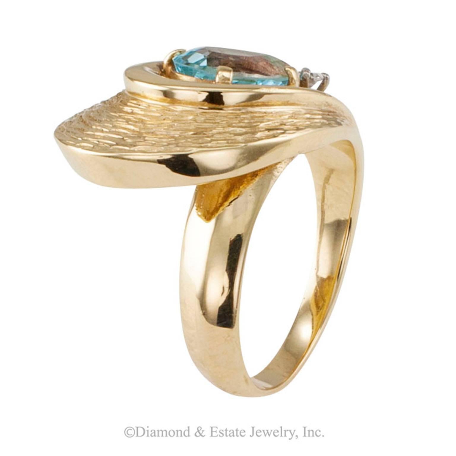 Modernist Blue Topaz and Diamond Cocktail Ring

A teardrop-shaped blue topaz and diamond cocktail ring with modernist lines, mounted in 14-karat yellow gold, circa 1960. Across the finger, swirling bands of textured gold wrap around a hollow motif