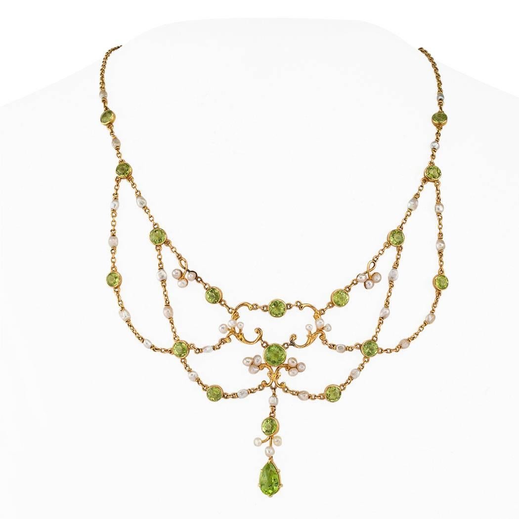 Antique 1900s peridot and pearl festooned gold necklace.  The festooned design features a delicate arrangement of bezel-set round peridots spaced at intervals between pearls, adorned at center front with reoccurring scrolling and foliar motifs