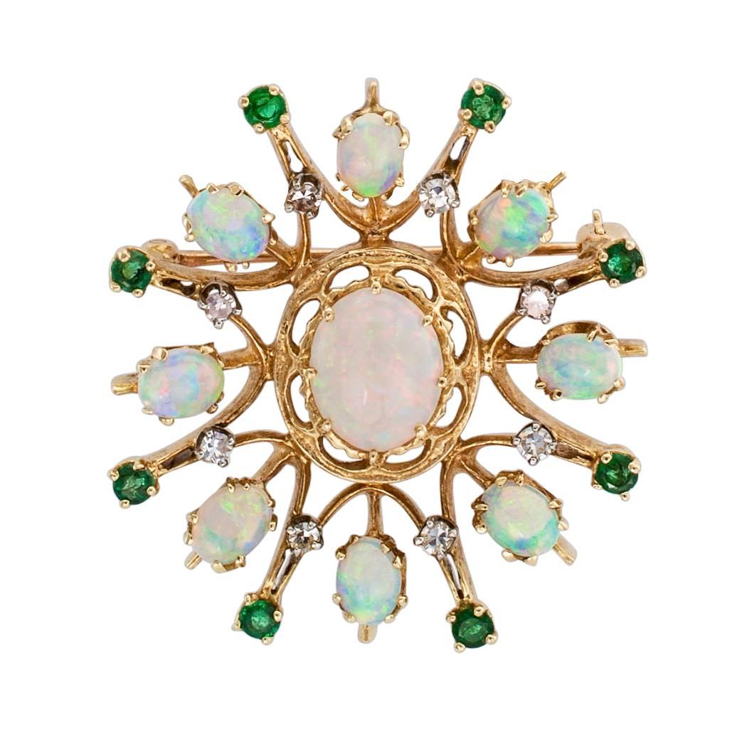 Opal emerald diamond and gold brooch pendant circa 1960. The sunburst design centers upon a larger opal framed by radiating motifs featuring smaller opals between eight sets of diamond and emerald pairs. The play of colors between the emeralds and