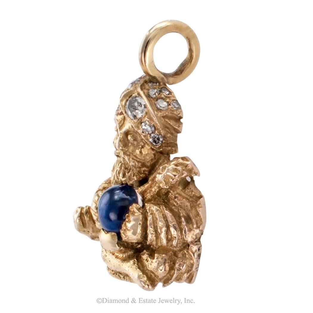 Mid century swami gold charm pendant set with sapphire and diamonds. The clairvoyant uses a cabochon blue sapphire as his divination crystal ball and his turban is frosted with fourteen diamonds totaling approximately 0.18 carat, mounted in 14-karat