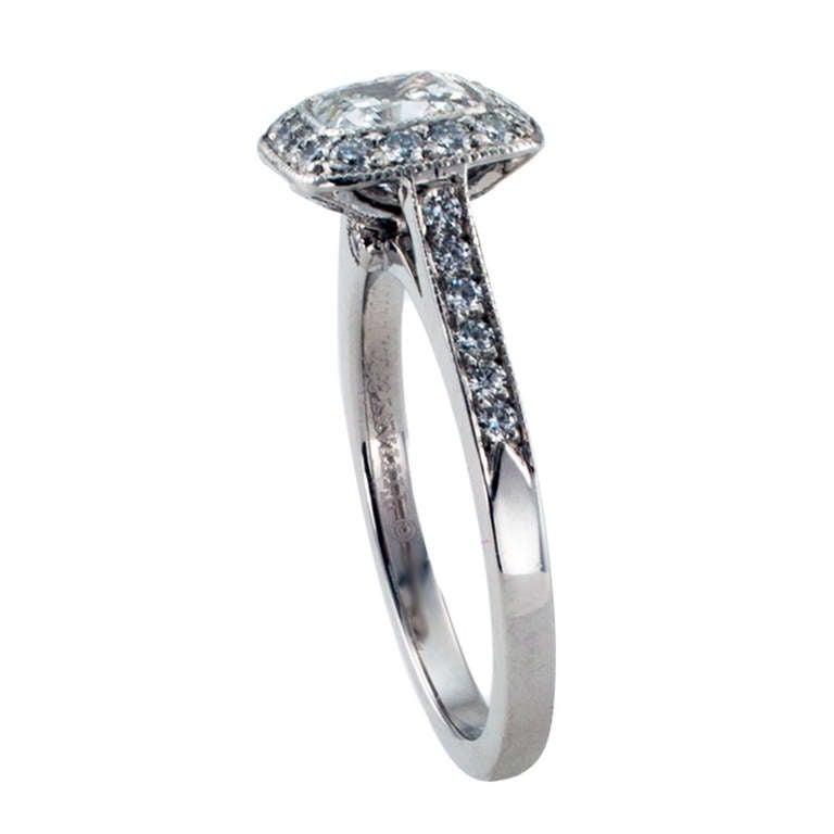 Centering upon a 1.00 carat cushion-cut diamond, within a conforming border of smaller round brilliant-cut diamonds, to the shoulders set with similarly cut diamonds, the open gallery decorated on each side by a single bezel-set diamond, accompanied