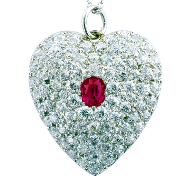 This beautiful Edwardian pave set heart pendant, tightly set with old mine and old circular cut near colorless diamonds totaling approximately 3.00 carats, approximately VS - SI clarity, H-I color, all cuddling to the central oval ruby weighing