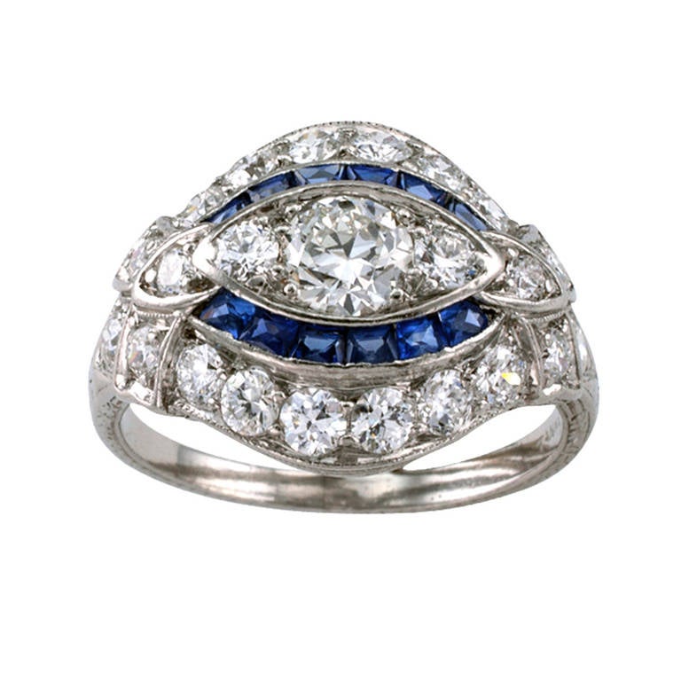 This wonderful slightly domed and beautiful band designed ring features a central diamond weighing approximately 0.40 carat, flanked by a pair of smaller diamonds, within a stepped border of French-cut blue sapphires and smaller circular-cut