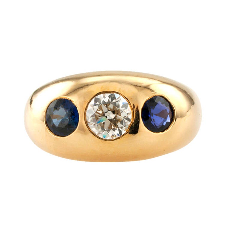 Dieser sehr traditionelle:: niedrig gewölbte Ring in Zigeunerfassung mit einem runden Diamanten von ca. 0::70 Karat (ca. Farbe H und Reinheit I1) zwischen einem Paar ähnlich geschliffener blauer Saphire ist in 14 Karat Gold gefasst:: 11 mm breit::