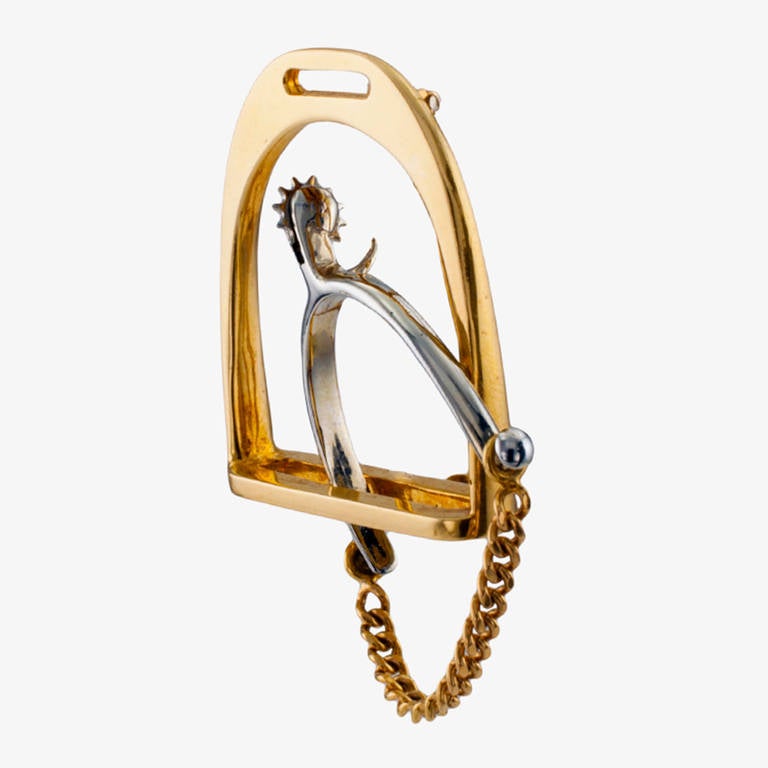 This great Hermes iconic and emblematic stirrup and spur motif brooch with an articulated rowel, is crafted in two-tone 18 karat gold, approximately 1 5/8" long  (including the chain spur support) by 11/8" overall. With French poincon