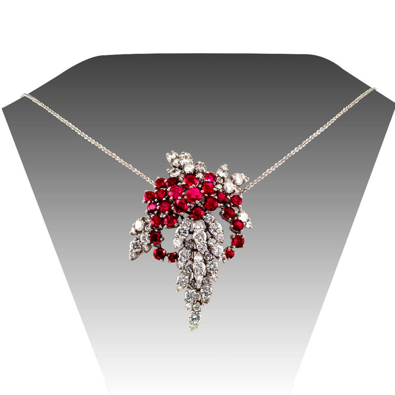 Ruby and Diamond Cascade Brooch-Pendant

Red rubies flashing against surrounding diamonds, a precious kindling that thrills and delights the senses.  Designed as a glamorous platinum brooch, the back fitted with two loops that permit threading a