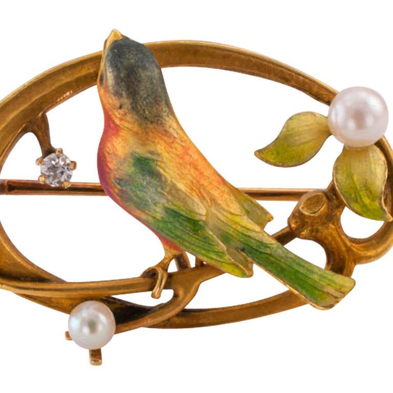 Circa 1905, this rare Art Nouveau brooch features a poly-chrome enamel bird, possibly a painted bunting, perched on a flowering  branch decorated with a small diamond and 3 pearls, made in 14 Karat Gold by Krementz.  That the bird appears to be