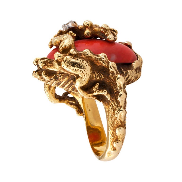 Circa 1960, this sensational vintage design composed by a most ferocious dragon clutching with the fierce strength of all its body onto an oval, richly colored, coral cabochon.  A small round diamond weighing approximately 0.06 carat sparkles from