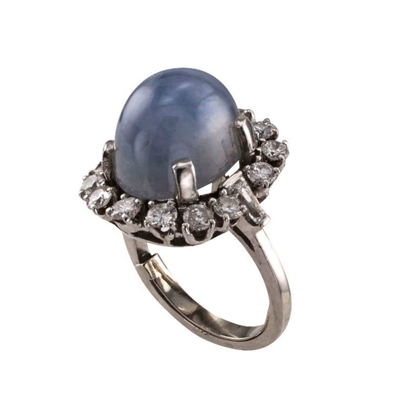 Circa 1950, this unique ring design showcases a very pleasing star sapphire with a very well defined star, weighing approximately 12.00 carats, in a classic heirloom mid 20th century platinum mount with tapered baguette shoulders and a border of