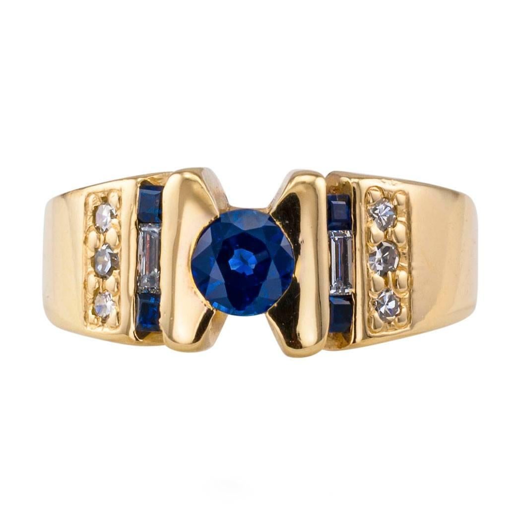 1970s Sapphire Diamond Gold Ring Band

Sapphire and diamond gold ring band circa 1970.  A single round blue sapphire enshrined within a half-bezel setting to shoulders that glisten and sparkle with additional calibrated sapphires, baguette and round