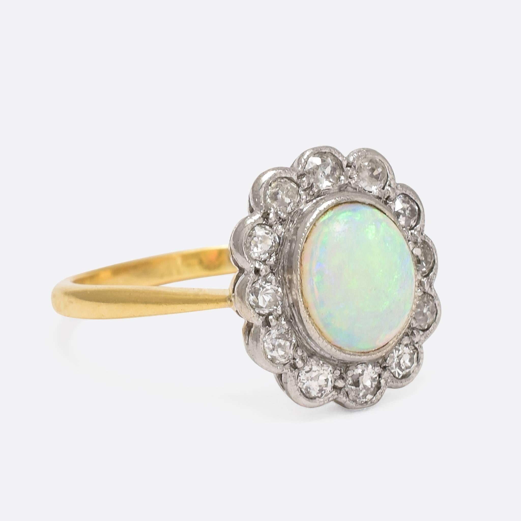 This beautiful antique flower cluster ring is modelled in 18ct gold and platinum, and set with a spectacular opal cabochon - bursting with colour and life - surrounded by a cluster of old cut diamonds. Fine millegrain detail accents the settings,
