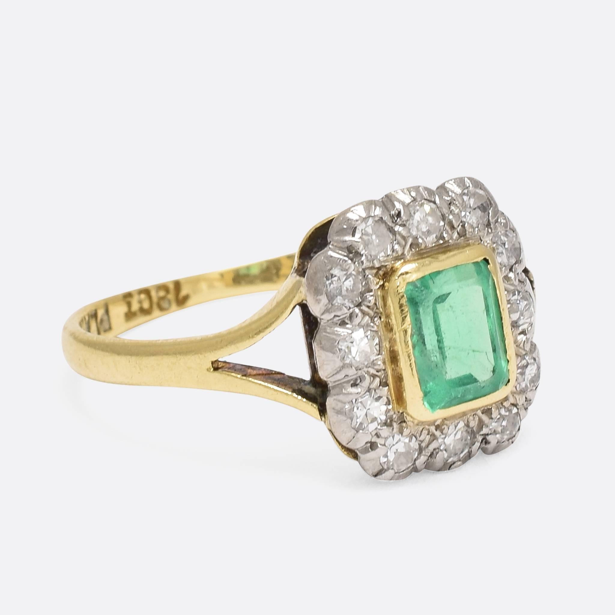 This superb antique cluster ring dates to the turn of the 20th Century. The central emerald is a striking vibrant green, in a gold rub over setting, while the diamonds are set in platinum. An open gallery and pretty bifurcated shoulders allow plenty