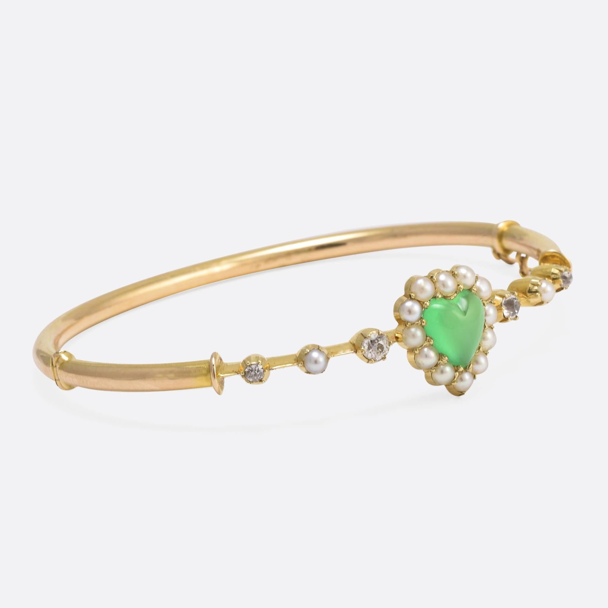 This attractive Victorian bangle features a heart-shaped head, set with a gorgeous apple-green chrysoprase cabochon surrounded by natural pearls. The shoulders are set with old mine cut diamonds, along with further pearls. Modelled in 15ct yellow