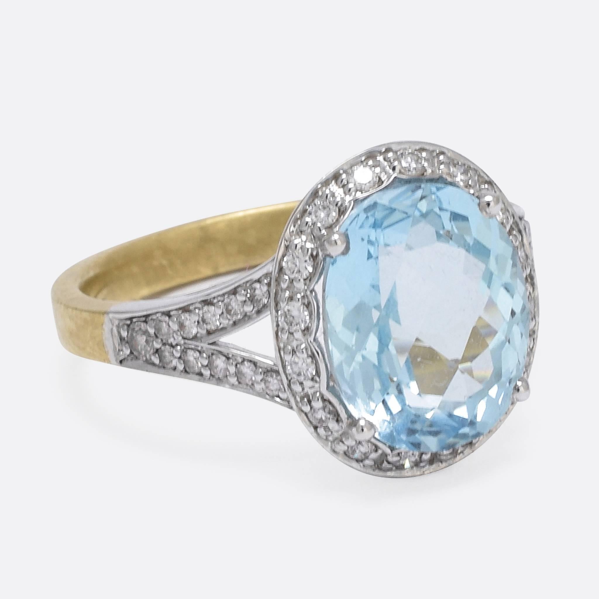This stunning contemporary cluster ring is set with a dreamy checker cut aquamarine, surrounded by a scalloped halo of white diamonds. The split shoulders are set with further diamonds, and a stylish open gallery allows the stone to be illuminated