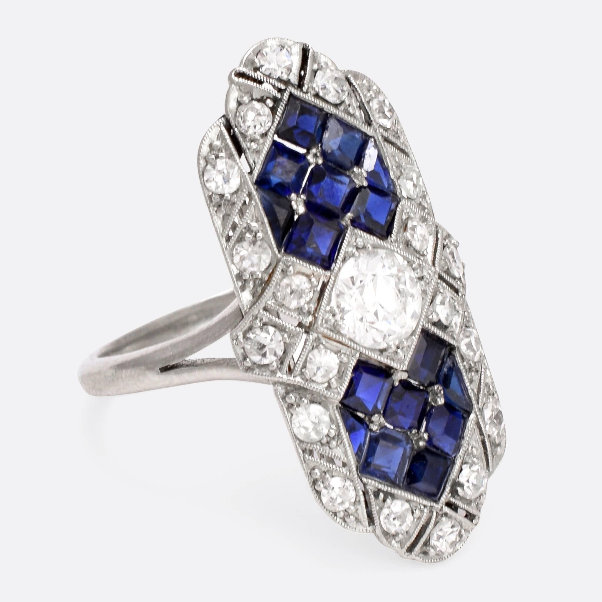 This stunning Art Deco era cocktail ring was made in France in the 1930s, modelled in platinum throughout. It's set with 16 vibrant calibre cut sapphires, and a cluster of diamonds - including a central .54ct old English brilliant cut. The head is