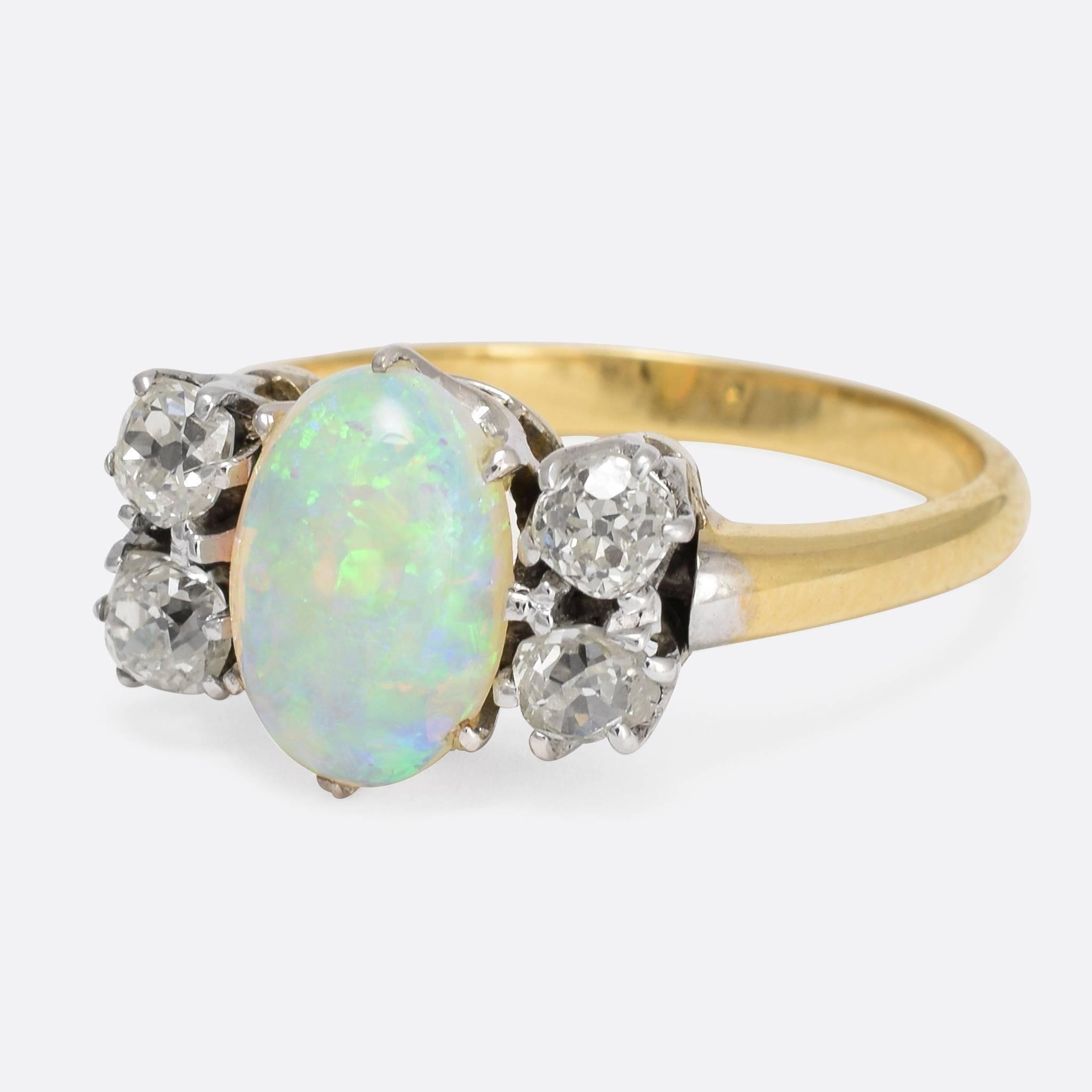 This unusual antique ring is set with a vibrant opal cabochon, flanked by two square cushion cut diamonds on either side. The stones are arranged very slightly offset from centre – held in platinum claw mounts. The simple band is modelled in 18k