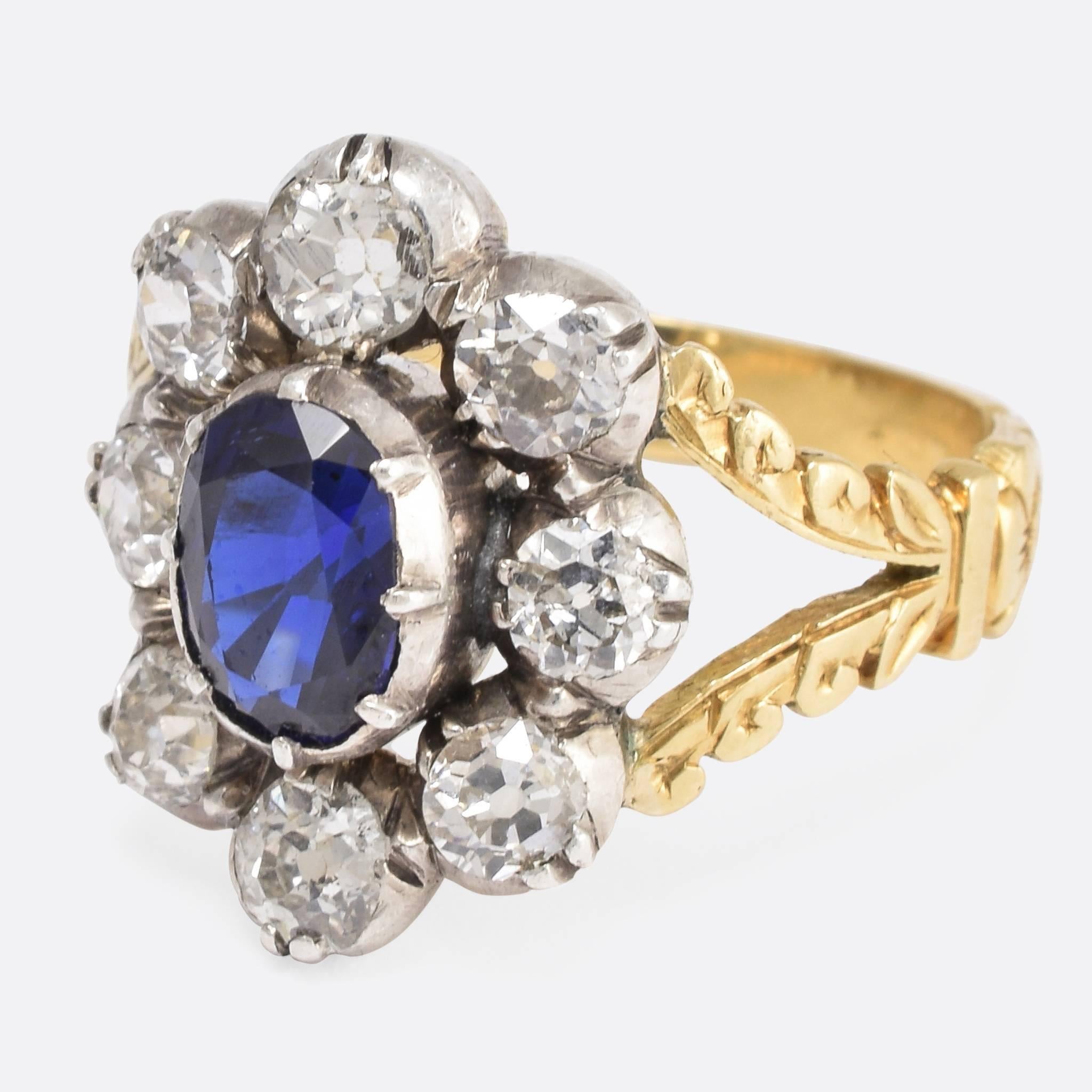 This stunning 19th Century cluster ring is set with a vibrant central blue Sapphire - likely of Burmese origin - surrounded by a 2.24 carat cluster of old European cut diamonds. The head is formed in a flower shape, and the elegant split shoulders