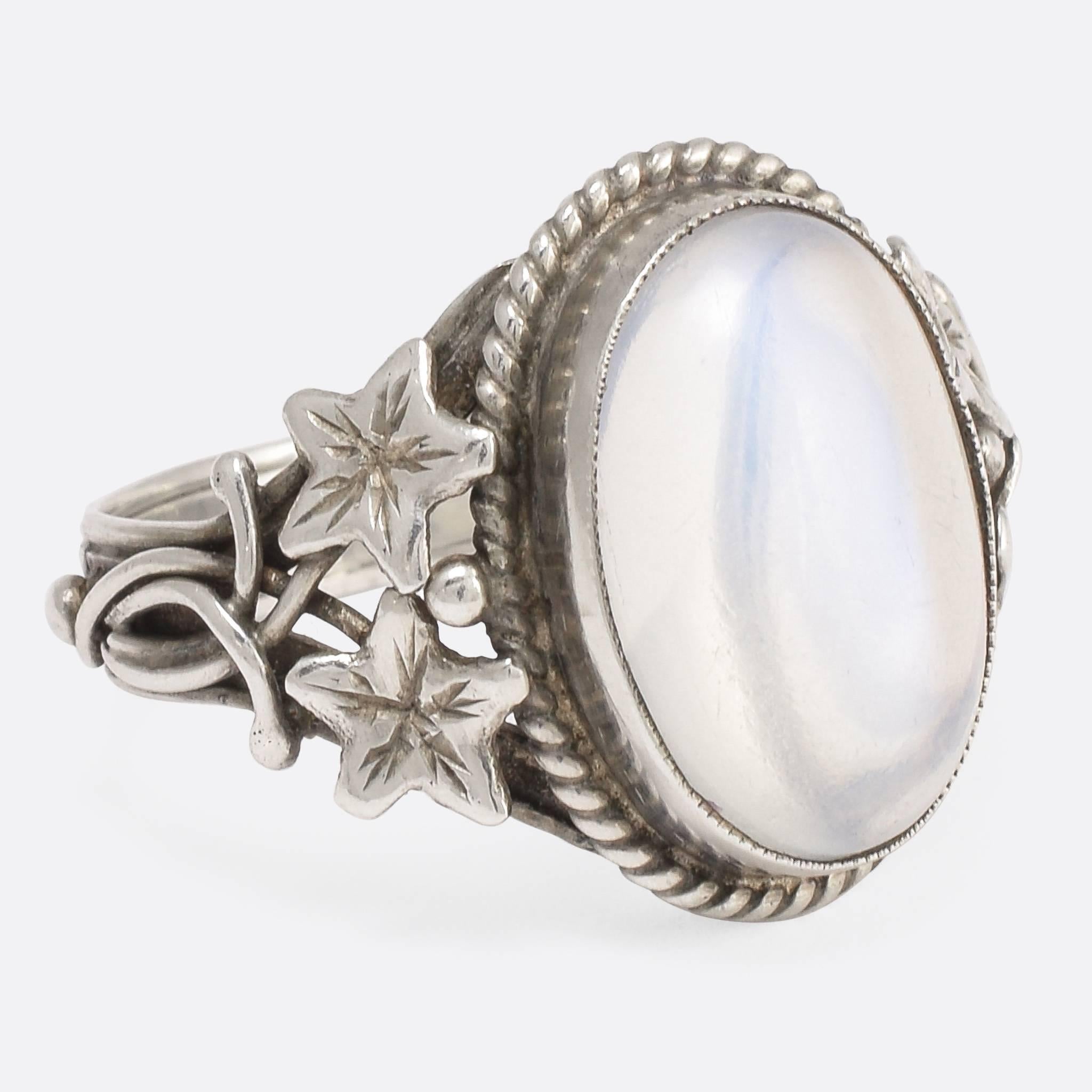 This attractive antique ring was made at the turn of the 20th Century in the Arts & Crafts style. It's modelled in sterling silver and set with a gorgeous oval moonstone cabochon - the shoulders feature delicate openwork foliate designs, and a