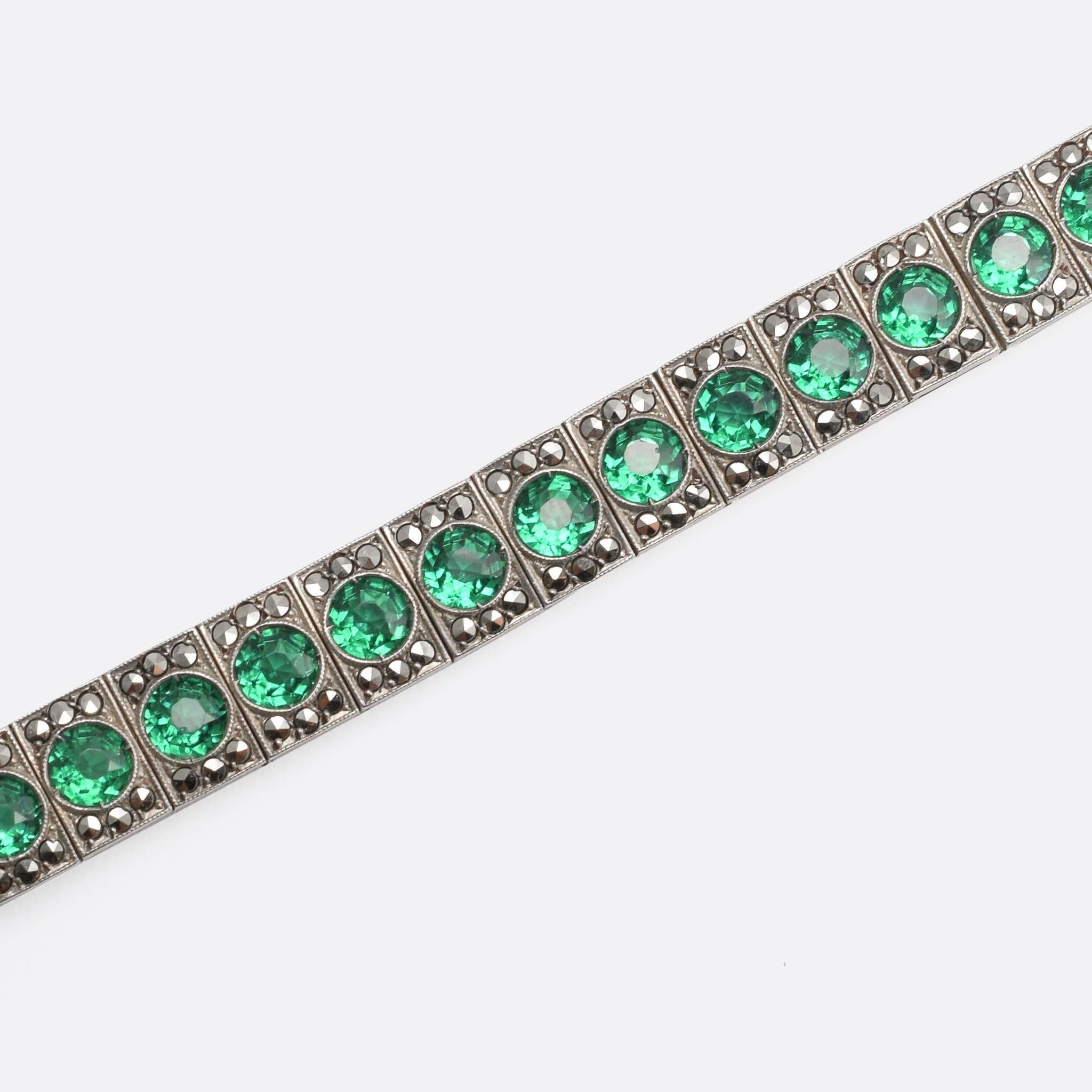 This stylish 1920s tennis bracelet is modelled in sterling silver, and set with 28 vibrant green paste stones - each accented with six faceted marcasite discs. In typical Art Deco fashion, the settings are finished with fine millegrain detail.
