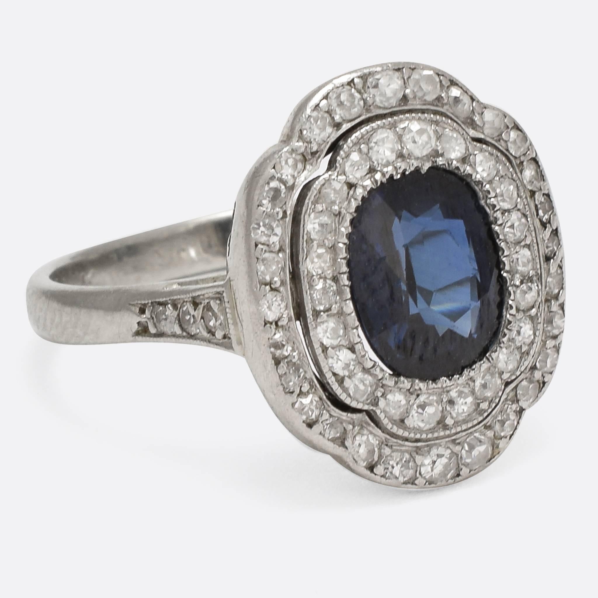 A stunning 1920s cocktail ring, set with a natural blue sapphire and a double halo of diamonds. The platinum settings are finely worked, with millegrain detail and diamond-set shoulders; while the back of the head features scrolled openwork. A