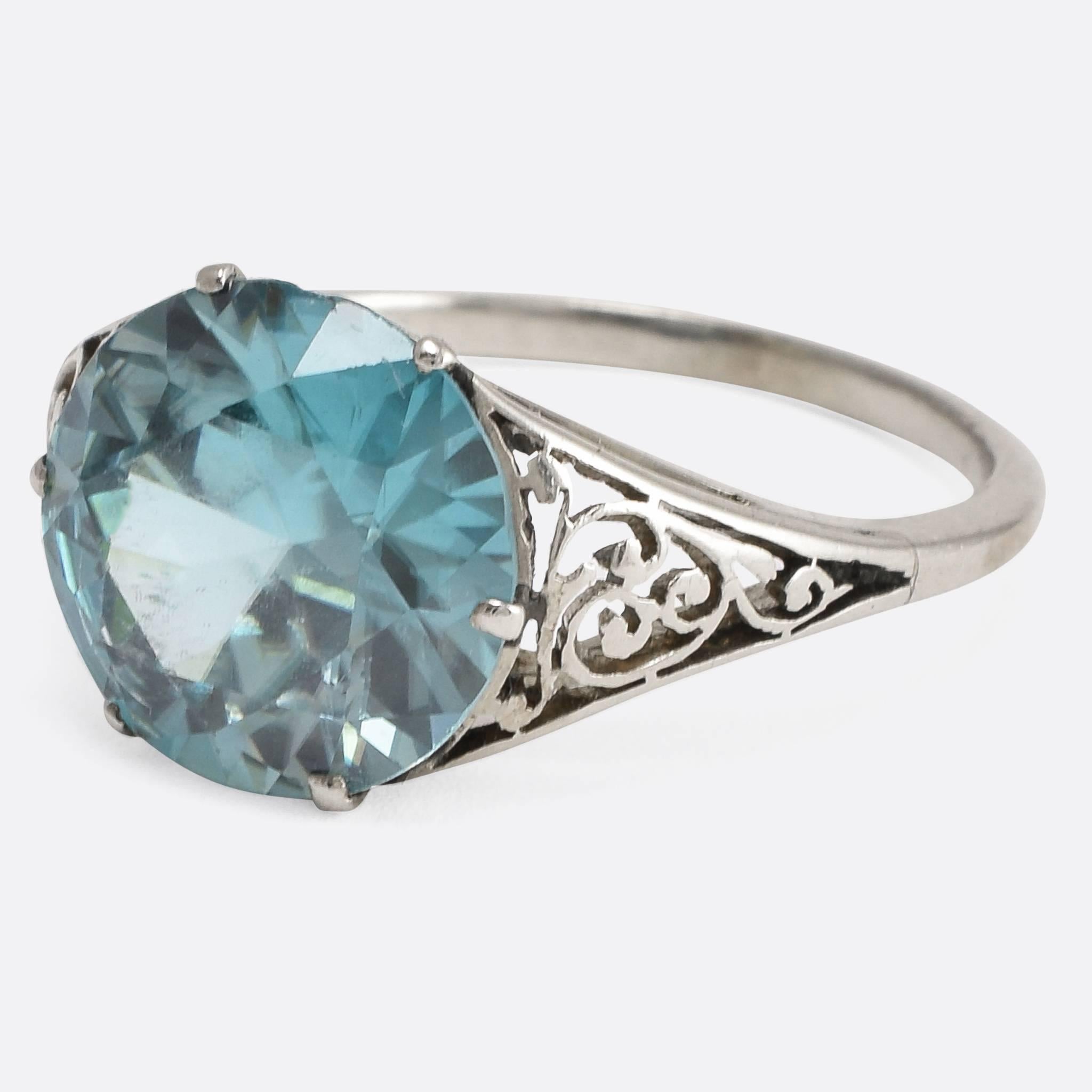 This 1930s solitaire ring is set with a vibrant 3.75 carat blue Zircon. The shoulders feature pretty filigree openwork and an elegant open gallery allows light behind the stone. The name zircon name derives from the Persian zargun, meaning 