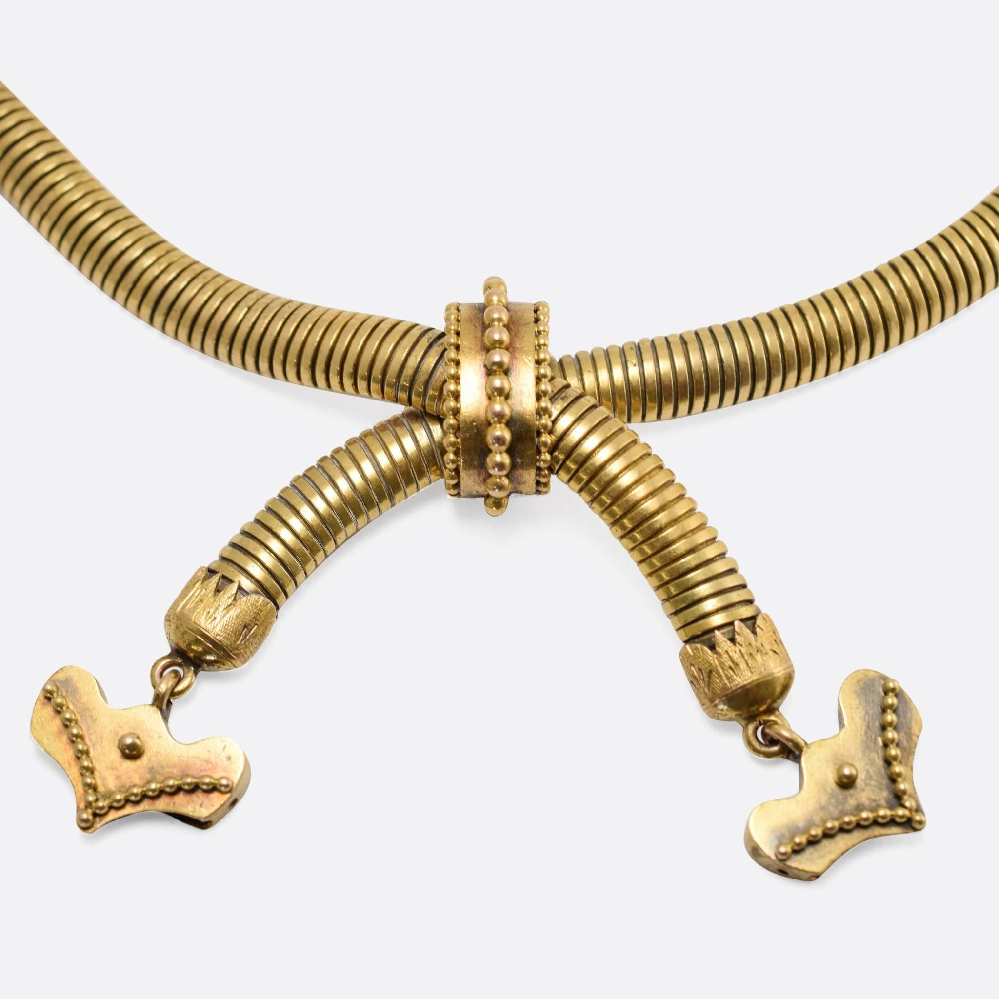 An excellent late 19th Century gaspipe collar necklace, modelled in rich 18k gold throughout. The gaspipe crosses over, held in place with a detailed gold hoop, and ending with stylized heart/arrow drops. A fine Victorian piece, dating to c.1890.