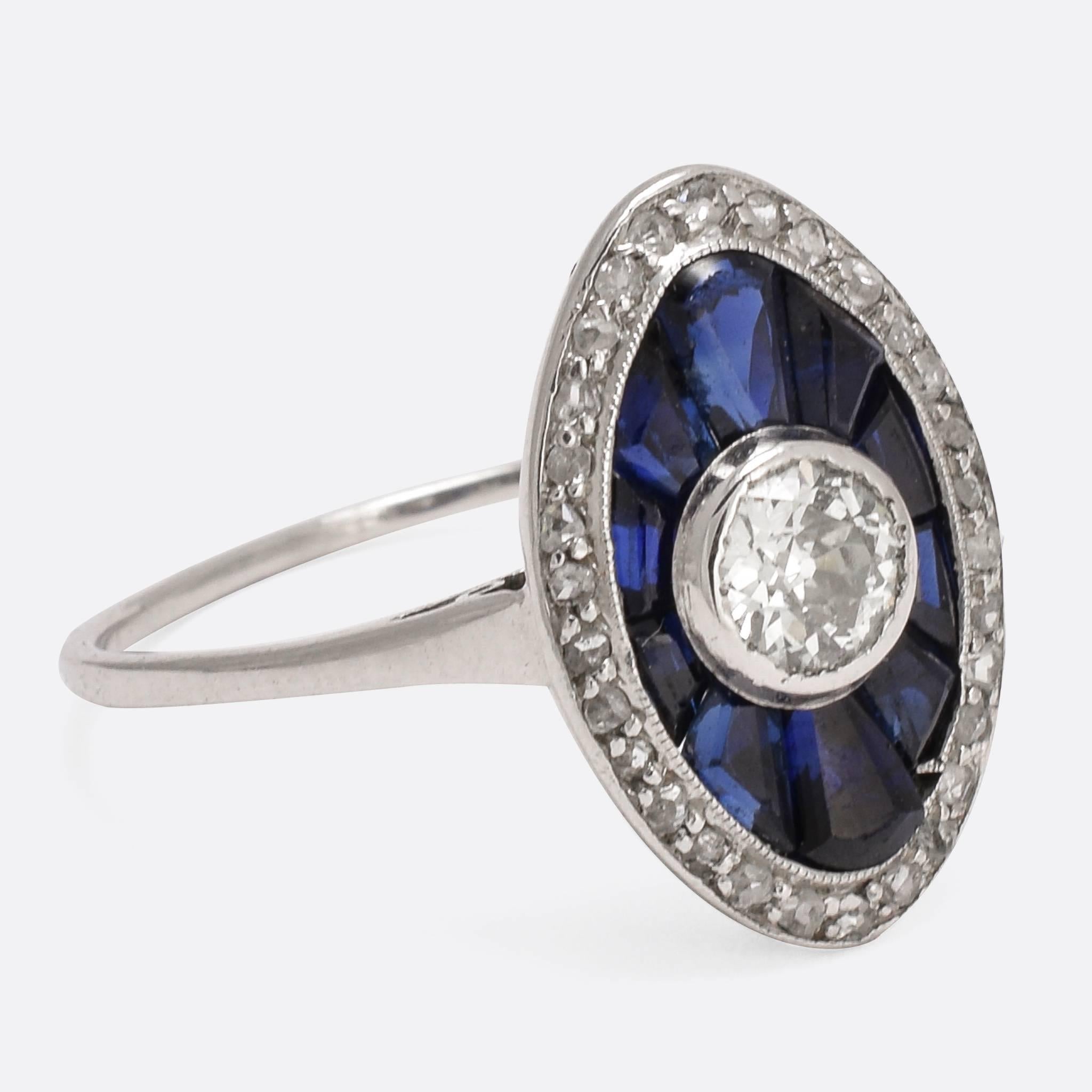 A bold 1920s sapphire and diamond cocktail ring, modelled in platinum throughout. With typical Art Deco styling, the head is set with calibre cut sapphires around a central .42ct old cut diamond. A further halo of diamonds completes the look, in