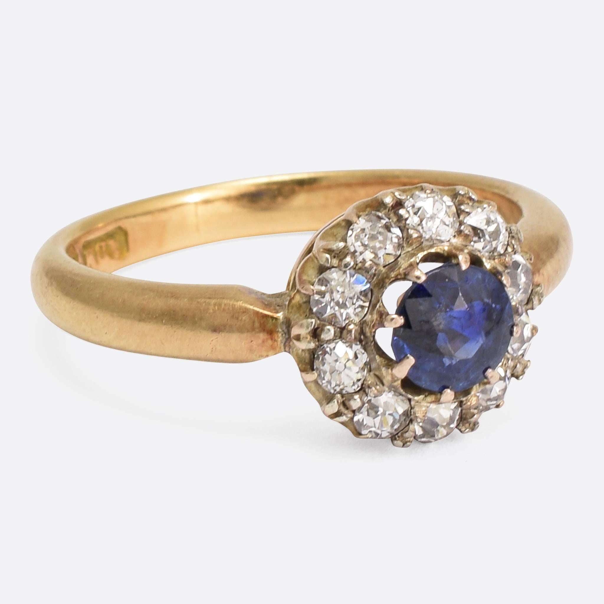 This pretty antique cluster ring is set with a central .50ct blue sapphire, surrounded by a halo of old cut diamonds. The round head has an open gallery, allowing light behind the stones, and the ring is modelled in 18k yellow gold throughout.