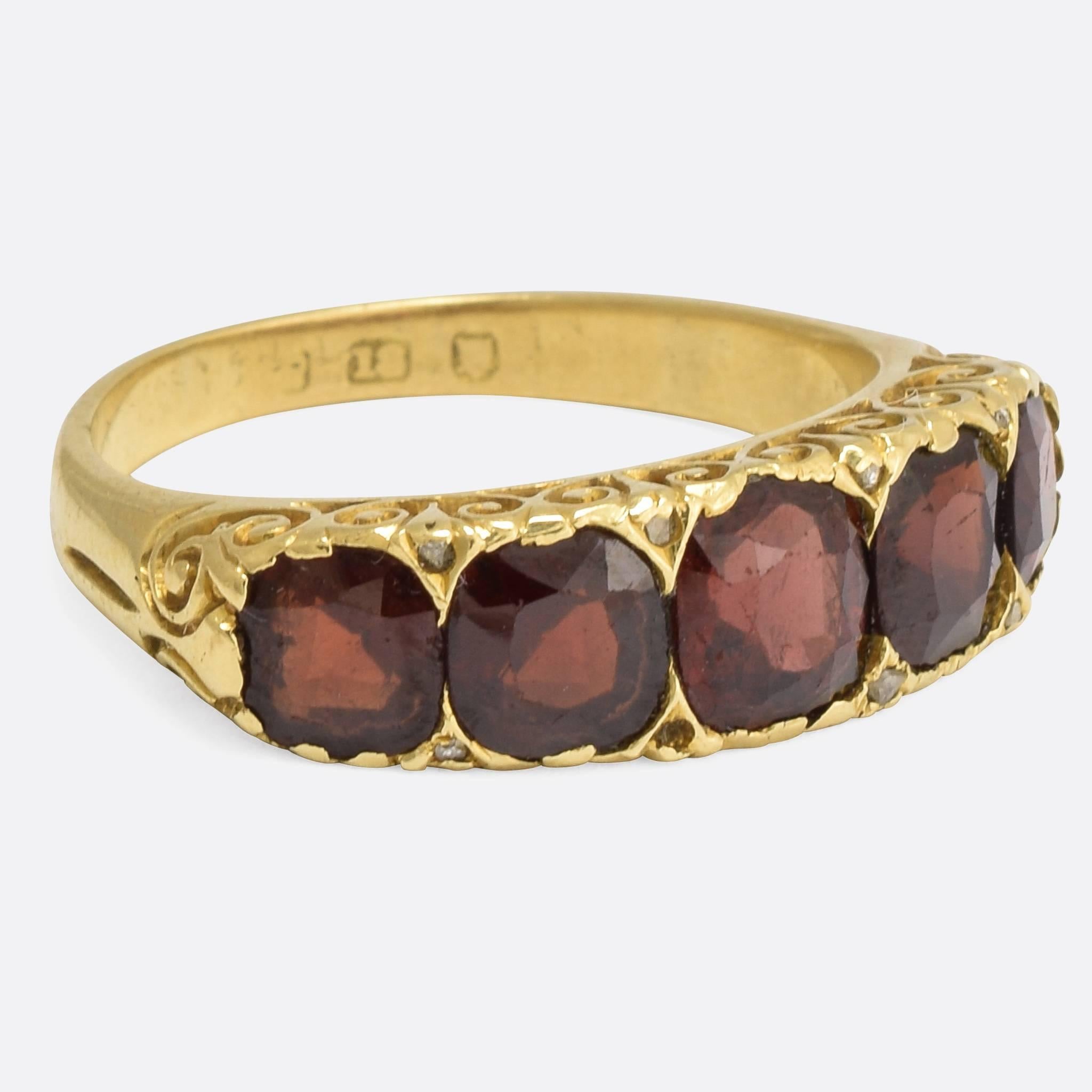 A cool oversized mid-Victorian 5-stone ring, set with five blood red garnets and tiny rose cut diamond accents. The gallery features deeply scrolled detailing that continues around the shoulders, and the mount is crafted from 18k gold throughout.