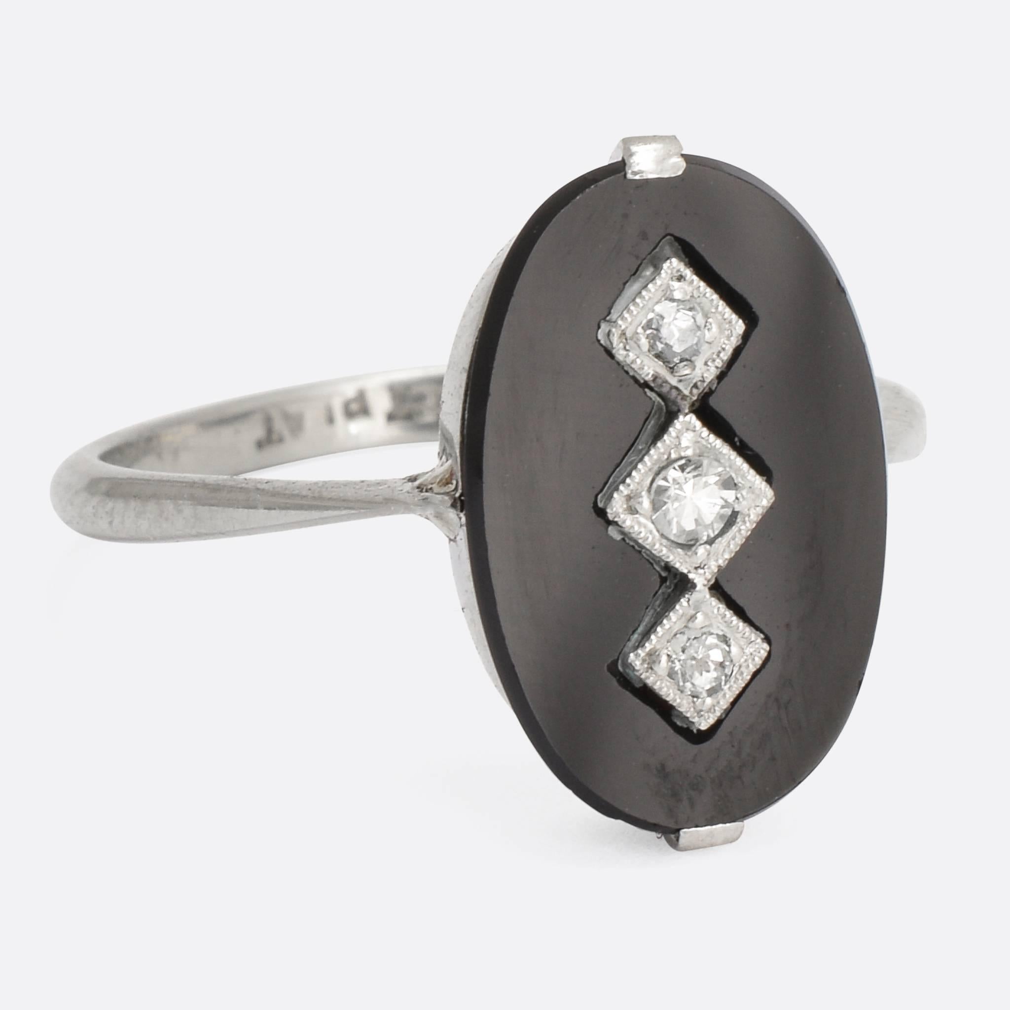 A cool Art Deco onyx and diamond panel ring, dating to c.1925. The three 8-cut diamonds glisten in millegrain settings, set into the oval black onyx panel; the whole head resting on elegant pinched shoulders. Modelled in platinum with an 18k white