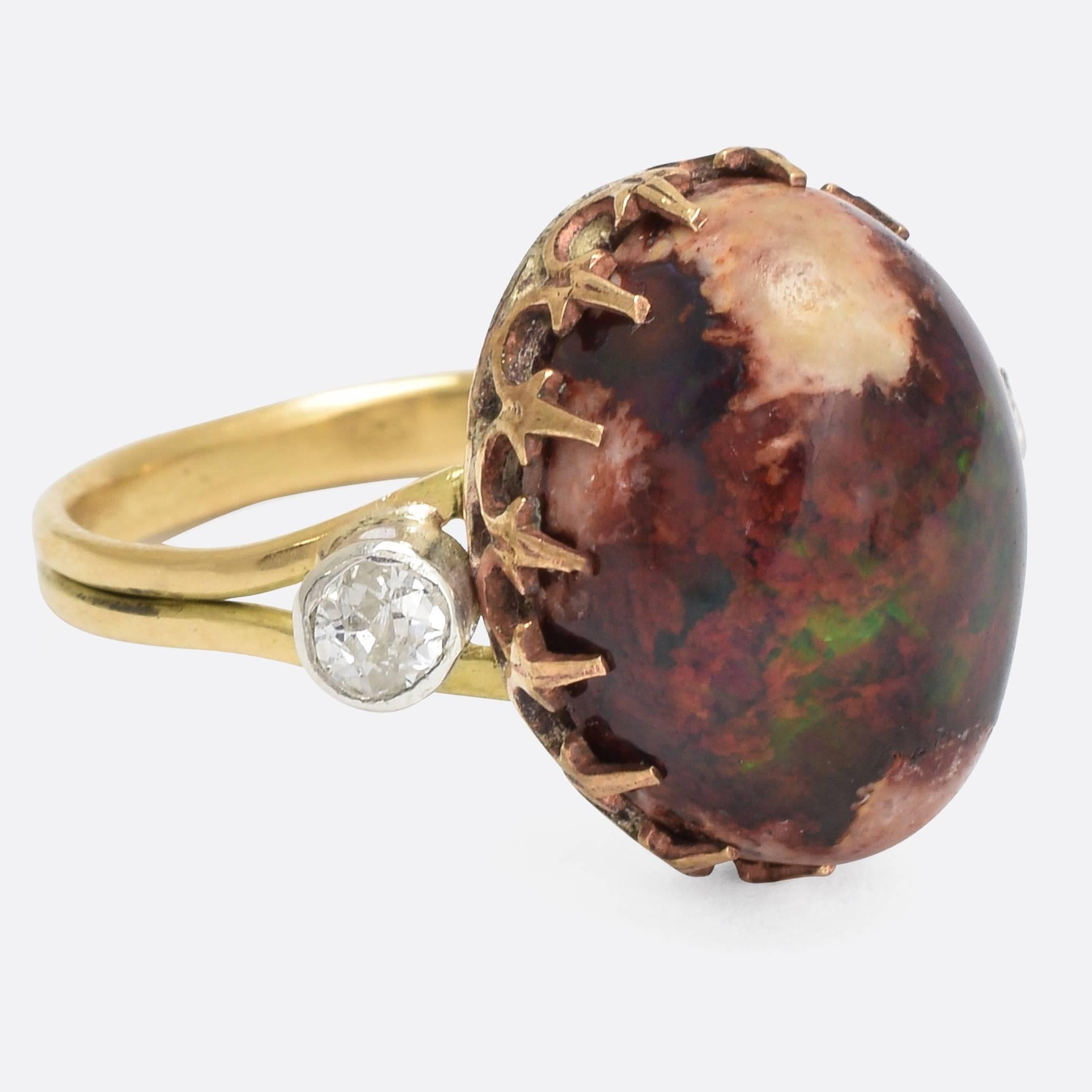 A stunning boulder opal is flanked by two old mine cut diamonds, in a highly attractive vintage ring mount modelled in 18ct gold throughout, the diamonds are intricately set in white gold collet settings, the band is reeded and tapers slightly from