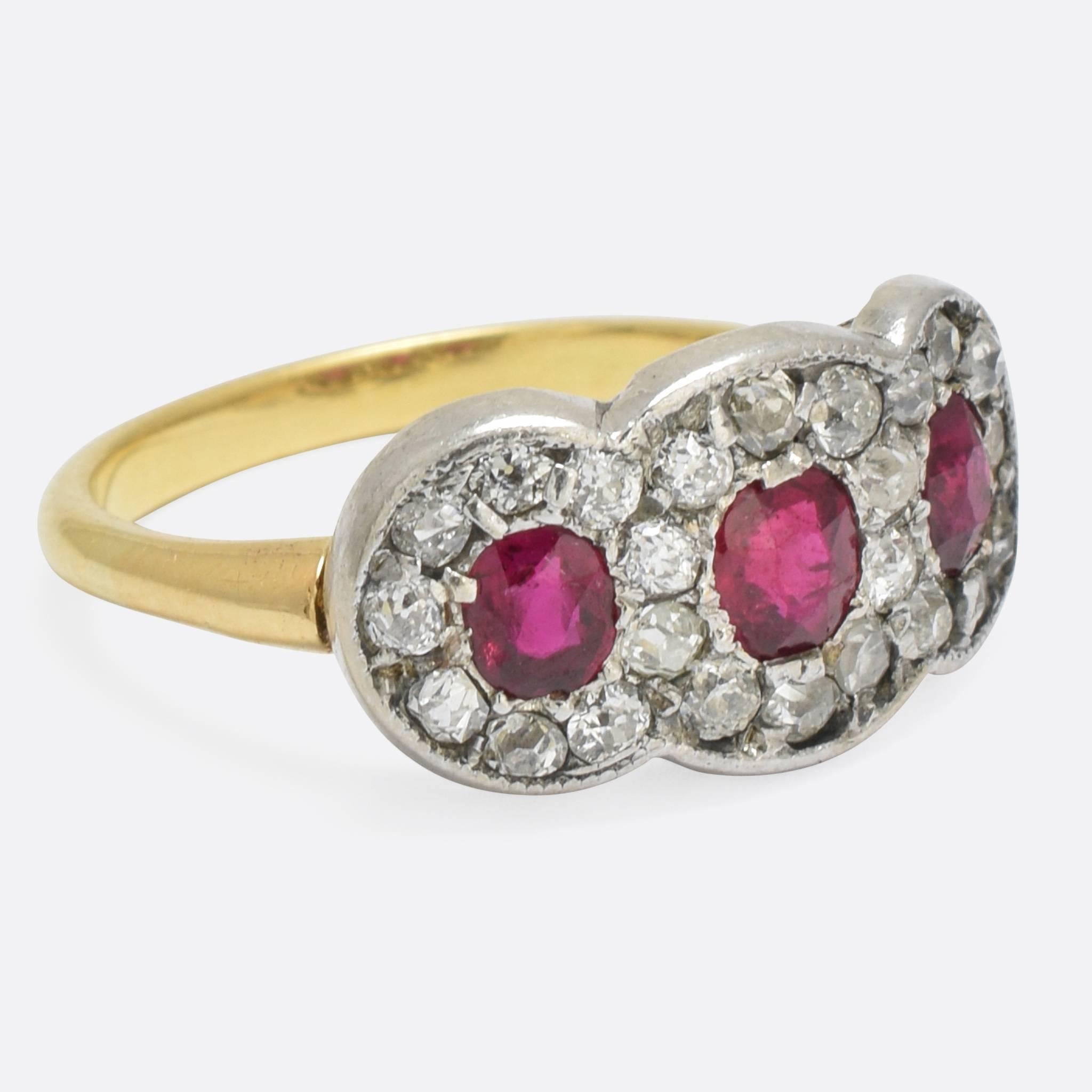 This wonderful antique three-stone cluster ring dates to the late Edwardian era, c.1910. Made in England, it's set with three blood-red rubies, within three interlinked halos of old cut diamonds. The plain band is modelled in 18k yellow gold, and