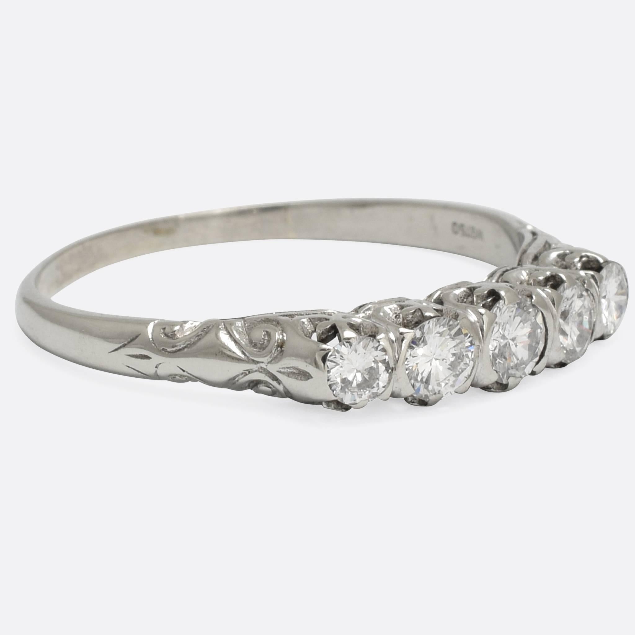 An elegant vintage engagement ring, set with five modern brilliant cut diamonds that total .56ct in weight. The ring has been modelled in the Victorian style, with hand chased scrolled detail to the shoulders and pretty trefoil claw mounts. Unusual