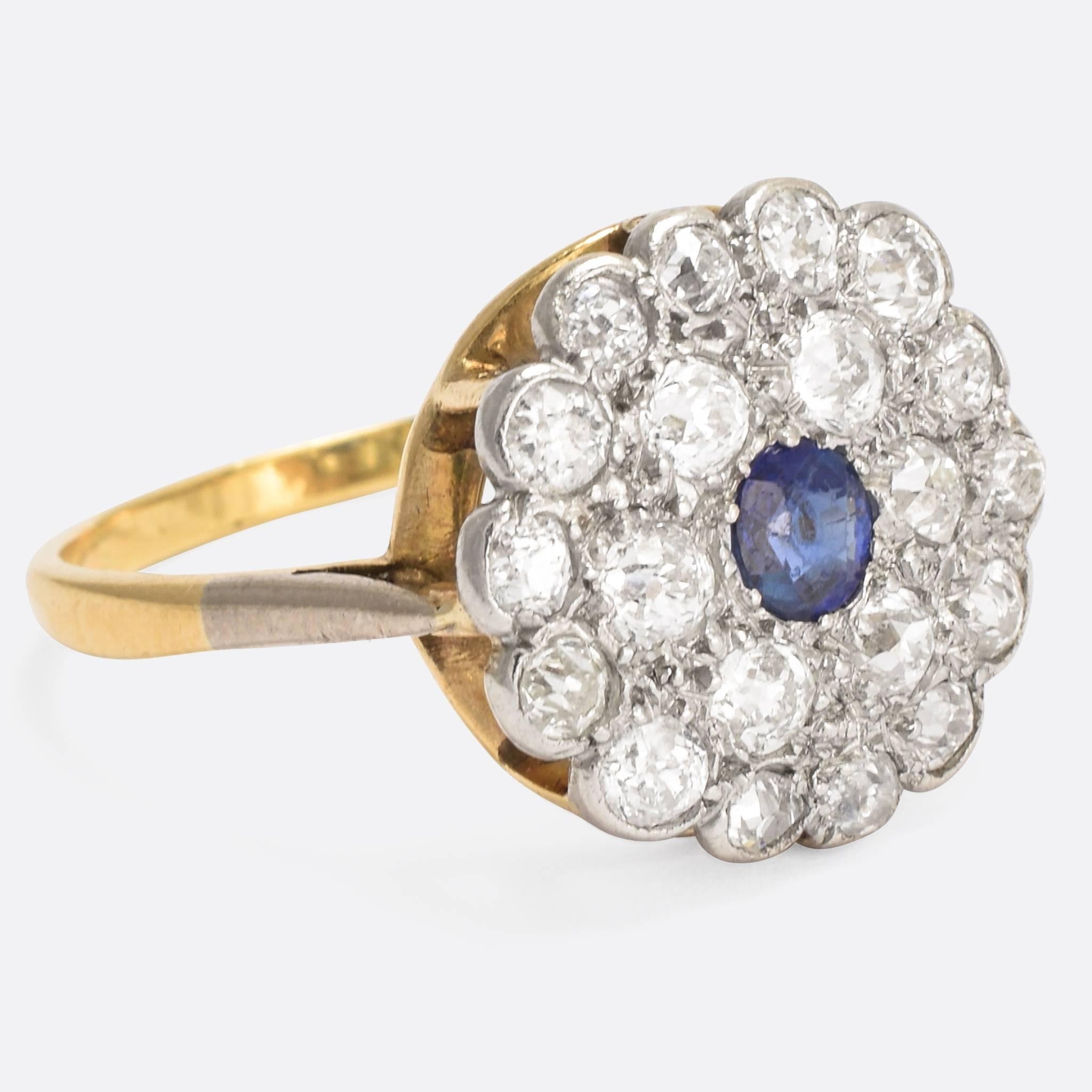 A beautiful Art Deco flower ring set with a central blue Sapphire surrounded by a double halo of old cut diamonds. It's modelled in 18k gold, with the stones mounted in platinum, which continues down the shoulders to create a stylish two-tone
