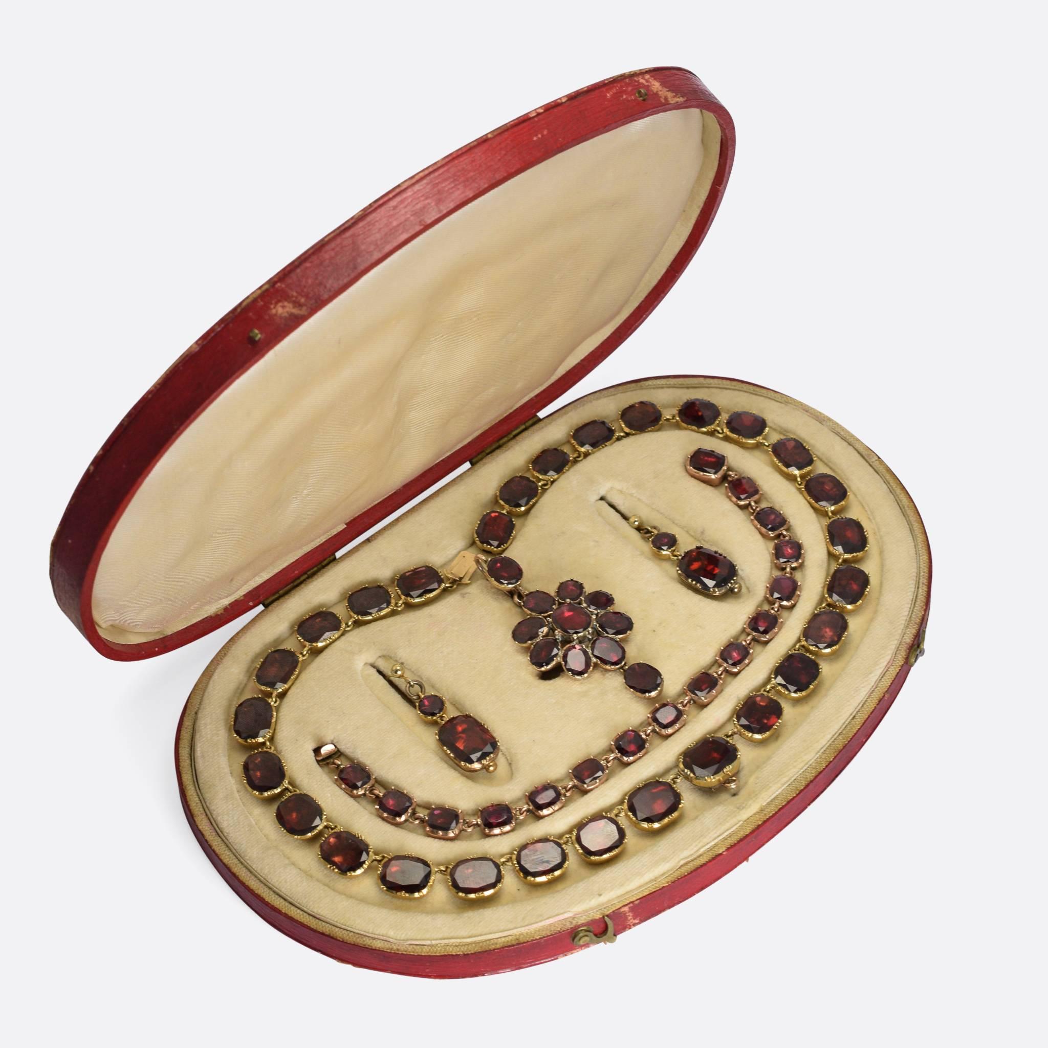 An extraordinary Georgian flat cut garnet suite, complete with original display box. It includes a full riviere necklace, a riviere bracelet, earrings, and a pendant that can also clip on to the necklace. The stones are bright with excellent colour,