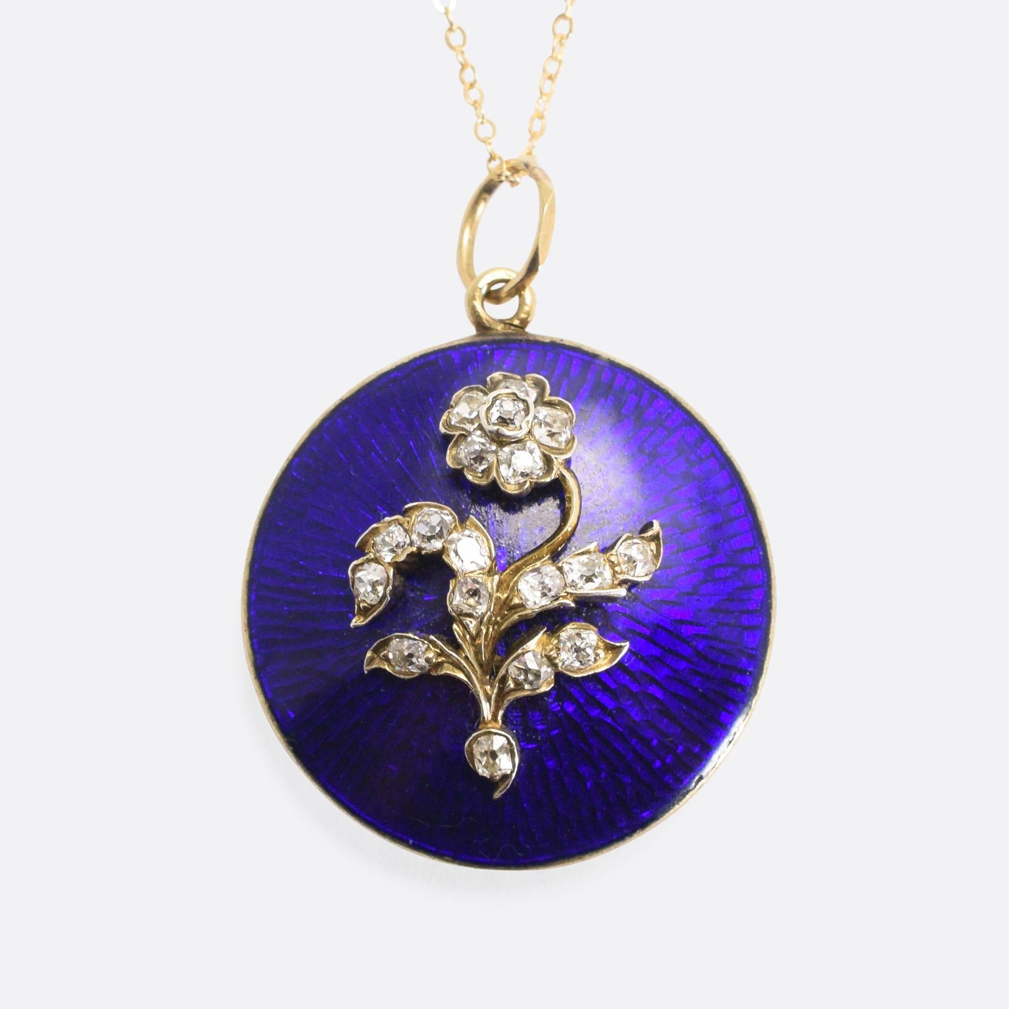 This beautiful round locket dates to the mid-Victorian period, circa 1860. The front features a diamond-set Forget-Me-Not flower on a sea of blue guilloché enamel. A glass-fronted locket compartment can be found on the back, with space for a