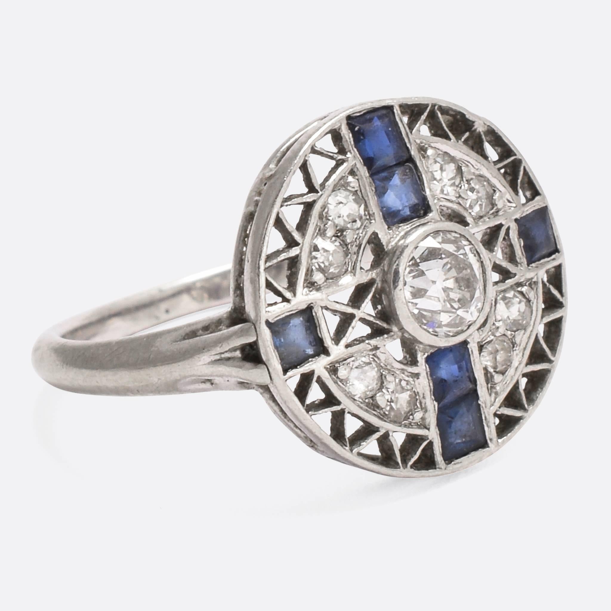 This superb Art Deco round cluster ring is set with six blue sapphires - in cross formation - and old cut diamonds. The head is intricately openworked, with triangular cut-out sections and crosses - all surrounding a central .20ct old European cut