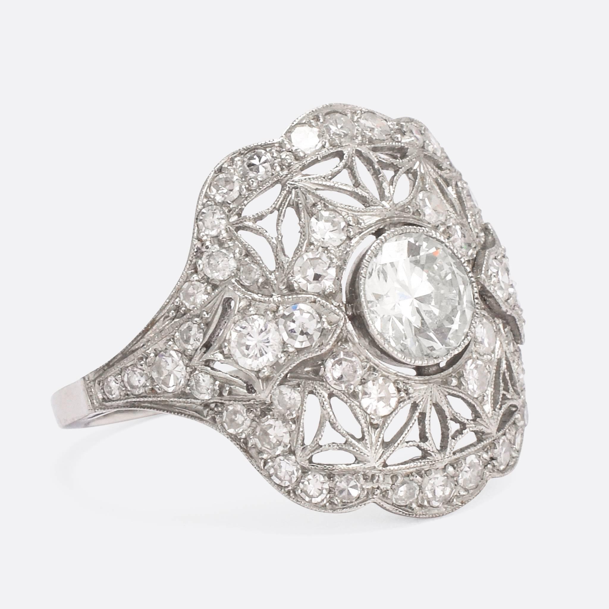 A stunning antique diamond cluster ring, featuring a wonderful delicately openworked head. The central stone is a clean and bright three-quarter carat transitional cut diamond, with an array of further diamonds all around it, set in millegrain. The