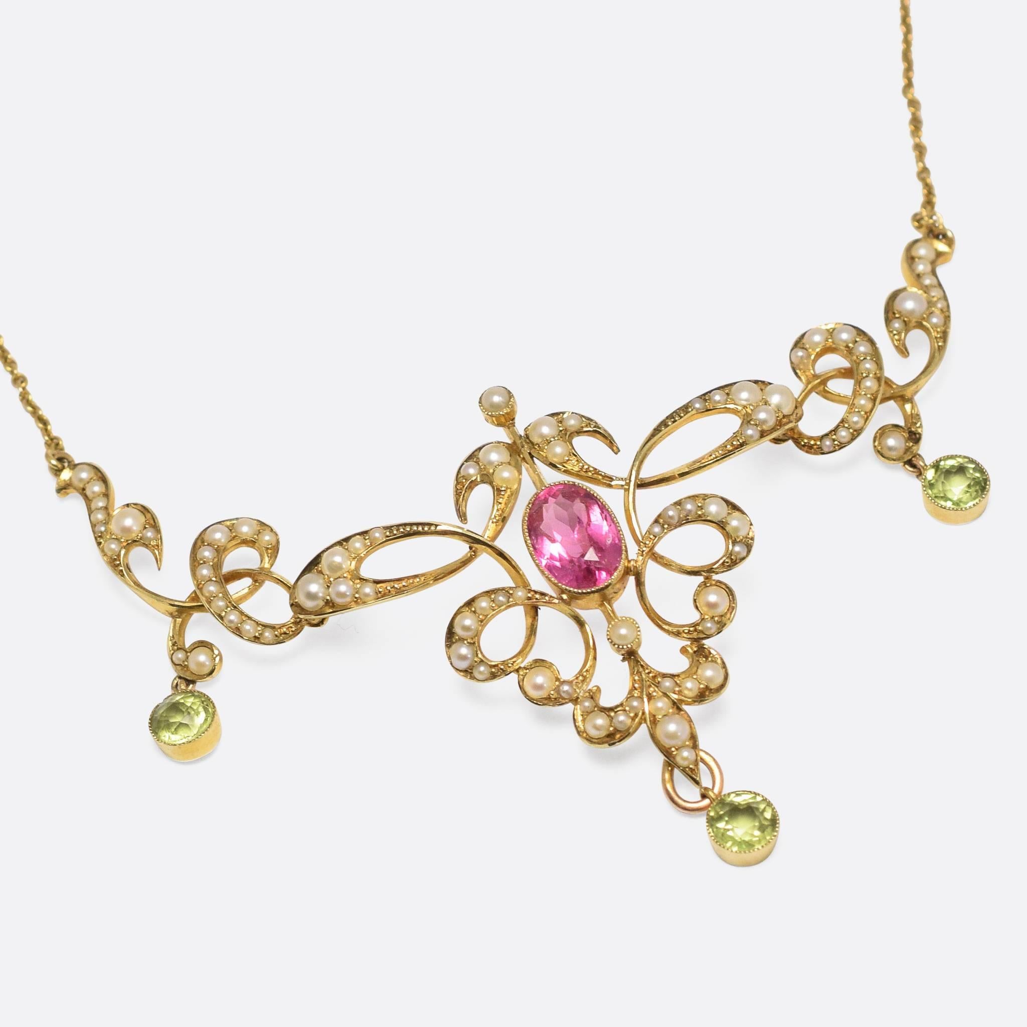 An impressive Edwardian era lavaliere pendant, set with peridot, pearls and a vibrant pink topaz centrepiece. The sides are articulated, moving freely beside the central body, and the piece features beautiful flowing foliate curves. Modelled in 15k