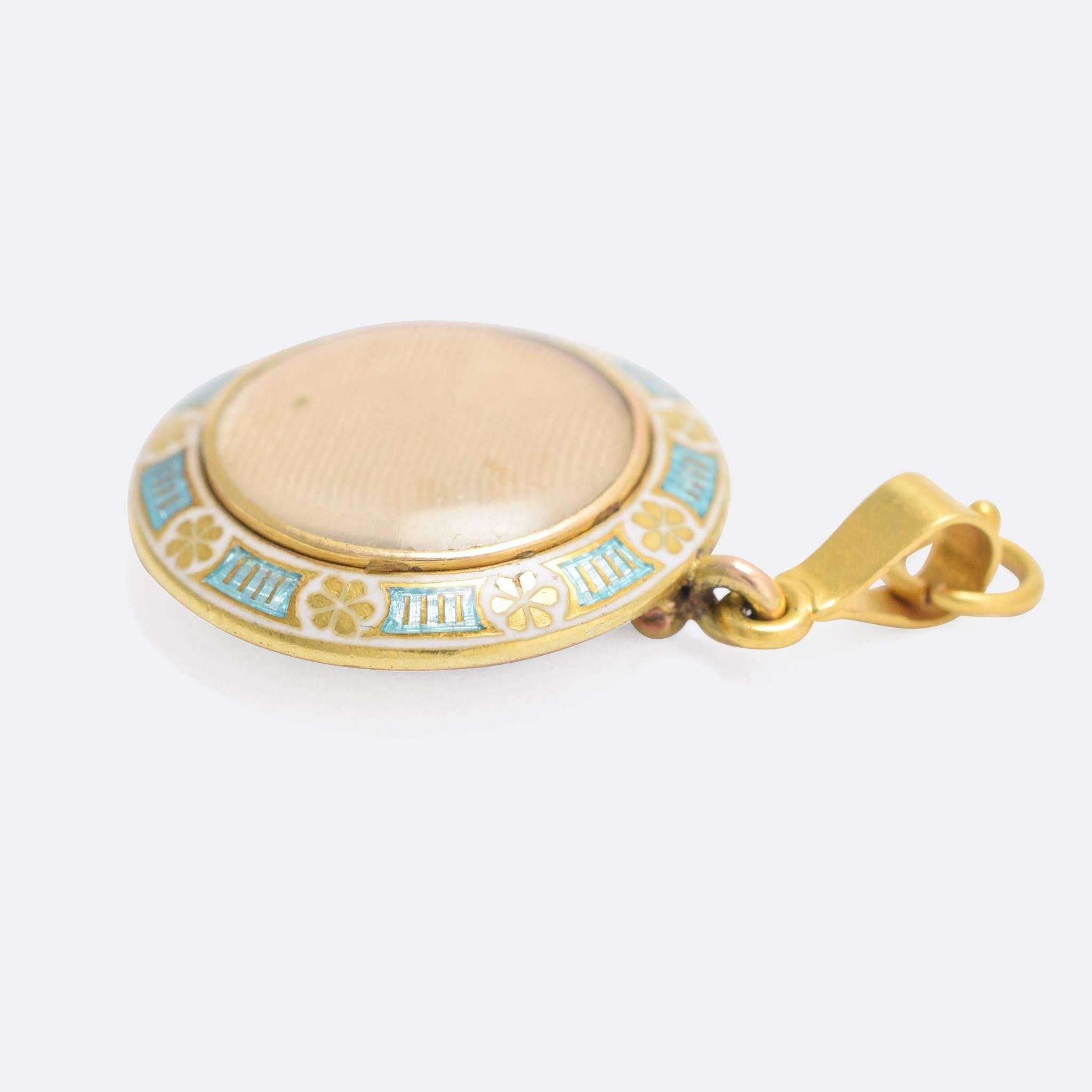 A beautiful antique round locket, by Child & Child of London. The front features exquisite enamelled border, in white and turquoise, around a central glass locket compartment. To the reverse, another glass compartment with an inscription dating to