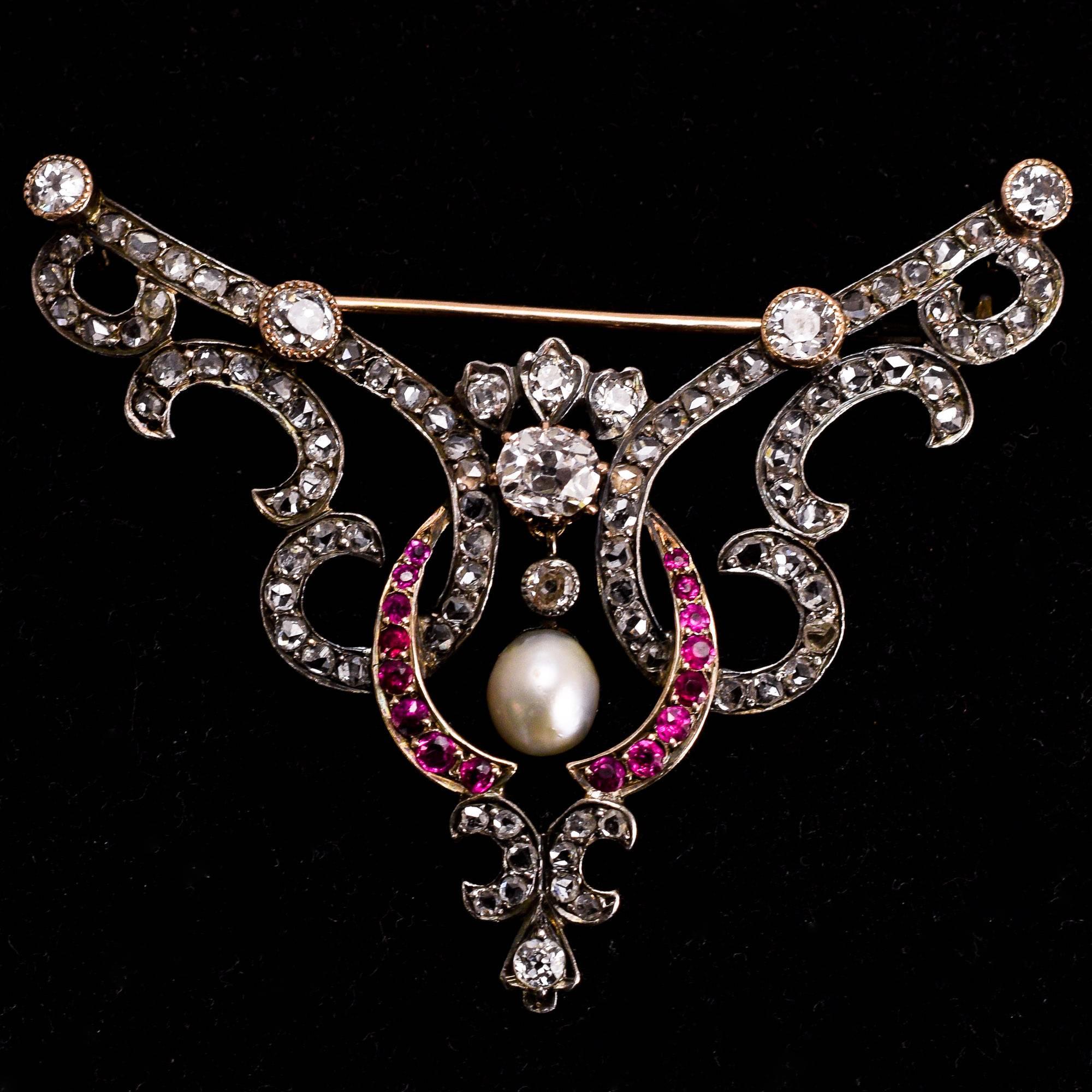 A glorious late Victorian brooch, set with diamonds, rubies, and an articulated natural pearl drop. It dates to c.1890, with graceful flowing curves, and an elegant form almost reminiscent of wings. The piece is set with around 2.8 carats of