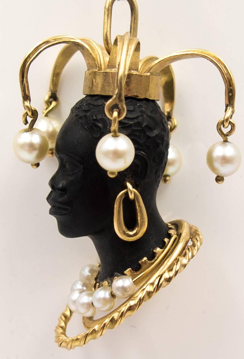 The highly elaborate headdress adorning this moor's head pendant makes it stand out from the crowd. The beautifully articulated face is framed by  a necklace of gold tubes and twists, anchored at the ears by large pendant hoop earrings, and crowned