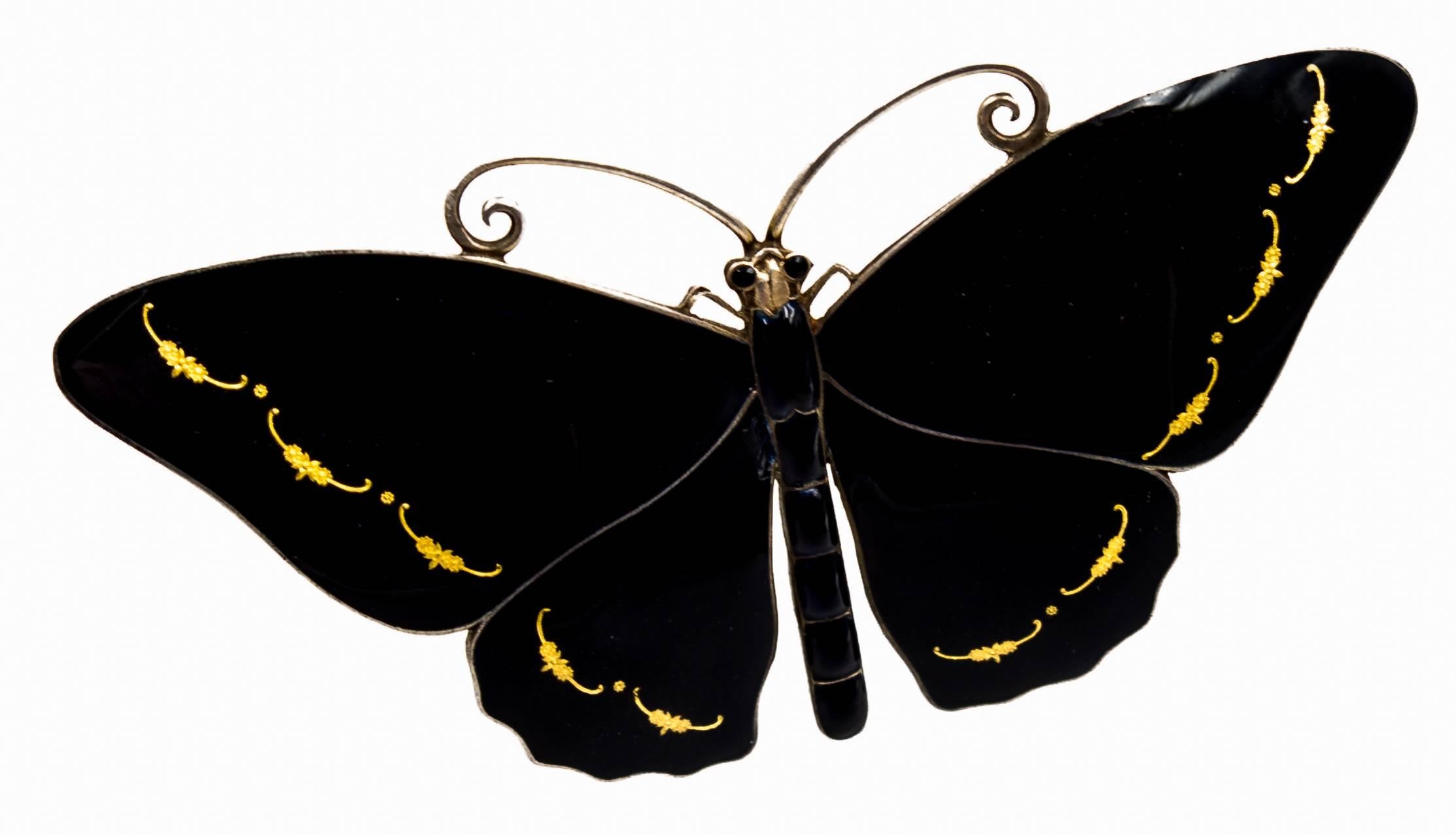 A ladylike and beautiful brooch crafted in silver, with lustrous black enamel wings accented at the edges with gold curlicues.   It measures 3 1/8" at its widest point, and 1 5/8" from top to bottom.  Many of the butterfly pins of this