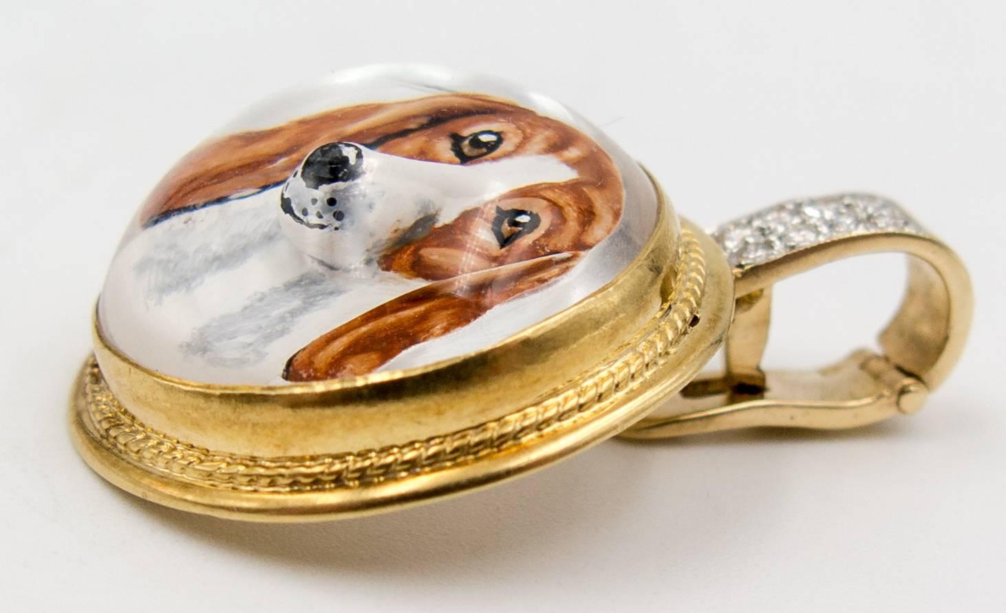 A charming hunting motif pendant consisting of a beautifully rendered brown and white spaniel painted on mother of pearl and topped with a dome of glass, set within a frame of 18 karat gold suspended from a pave diamond clip  bail (8 modern