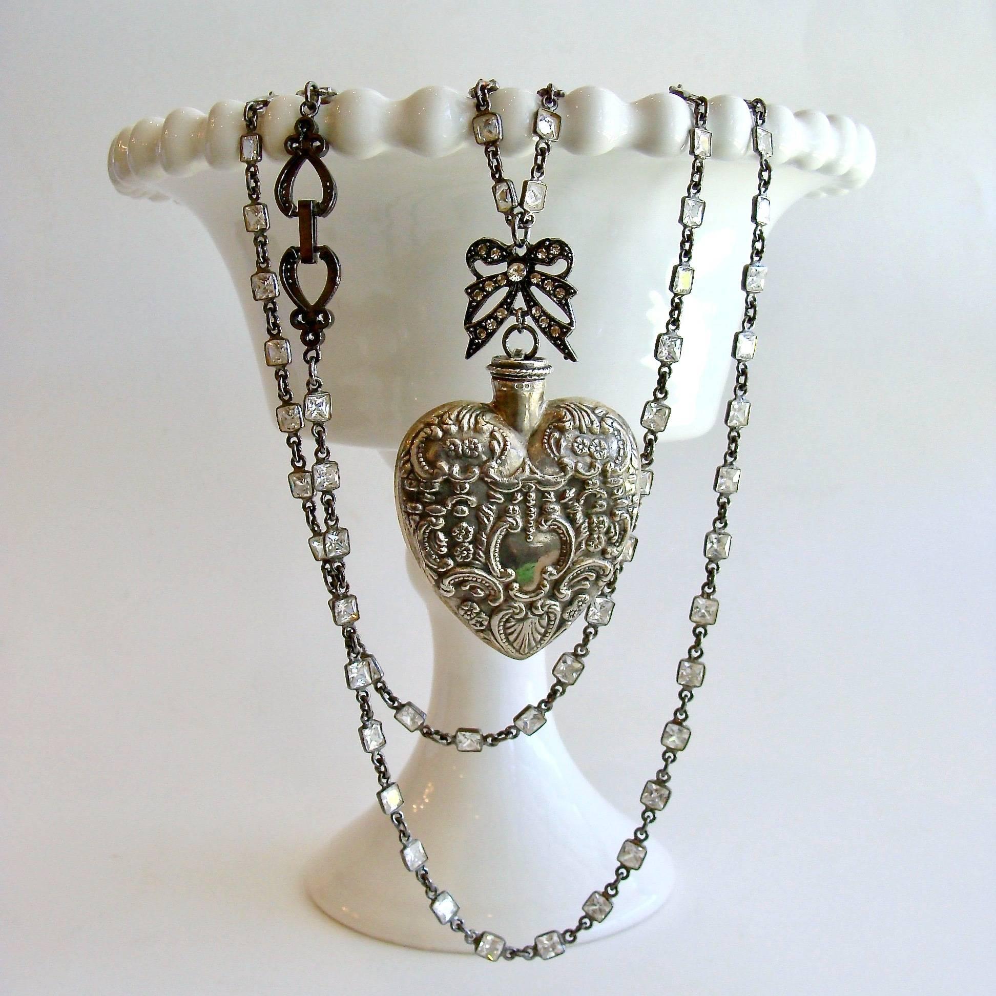 Cressida Necklace.

A lovely antique sterling silver repousse chatelaine heart scent bottle is the focal point of this beautiful layering necklace.  A charming rhodium silver paste bow presides over the top of the feminine heart shaped bottle, while