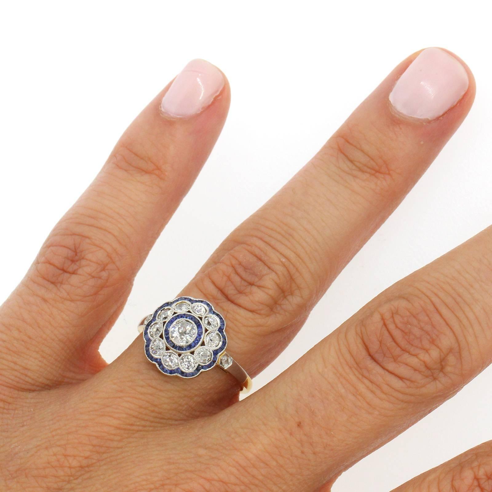 A vintage cluster design ring fabricated in platinum top and 18KT yellow gold centering an Old European Cut Diamond of approximate 0.30 carat.  The ring is accented with calibrated blue Ceylon Sapphires and ten Old Cut Diamonds.  The sides of the