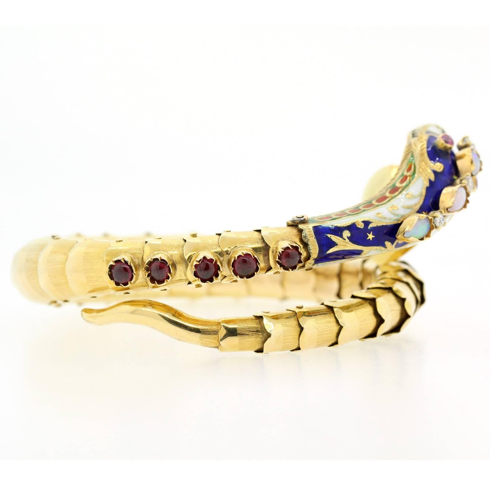 A splendid 1960s coiled snake blue enamel bracelet.  The 18KT gold snake has f flexible scales and a body accented with blue and white enamel, red Ruby eyes, Opals,  cabochon cut Garnets, and three Old European Cut Diamonds.  A dangling offering